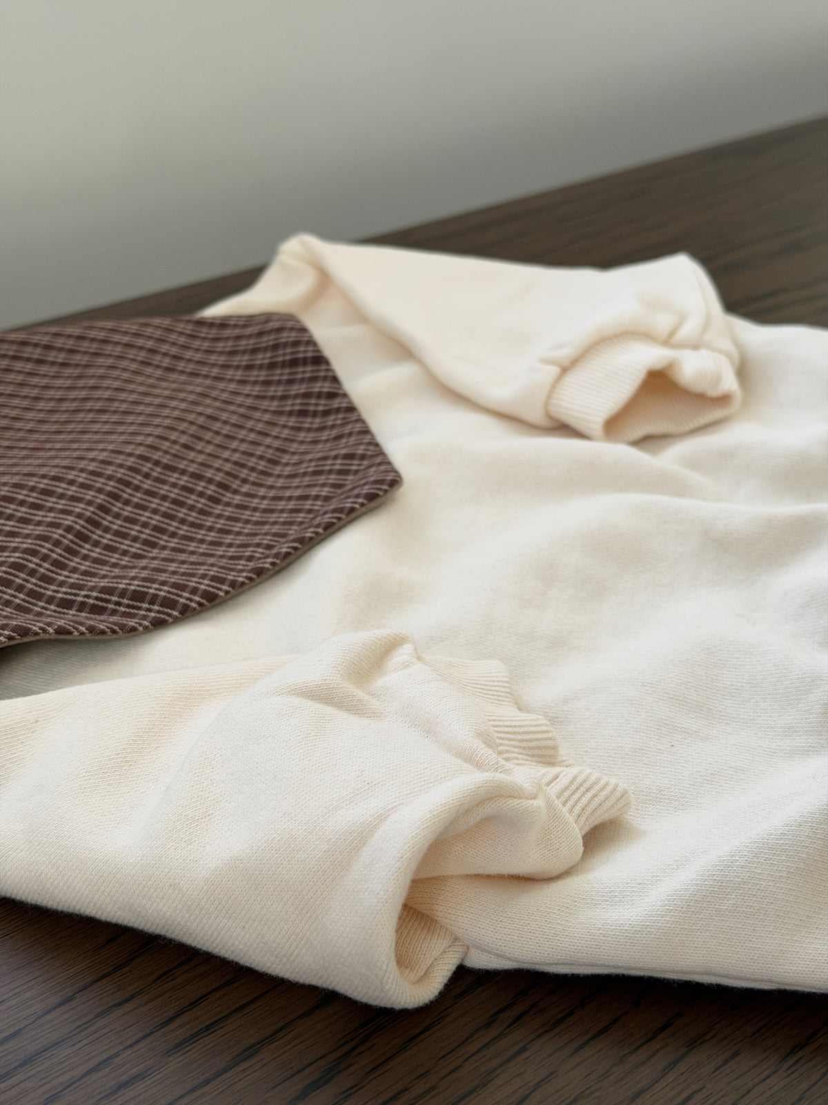 Cream crew-neck sweatshirt for baby laid out with checked bib