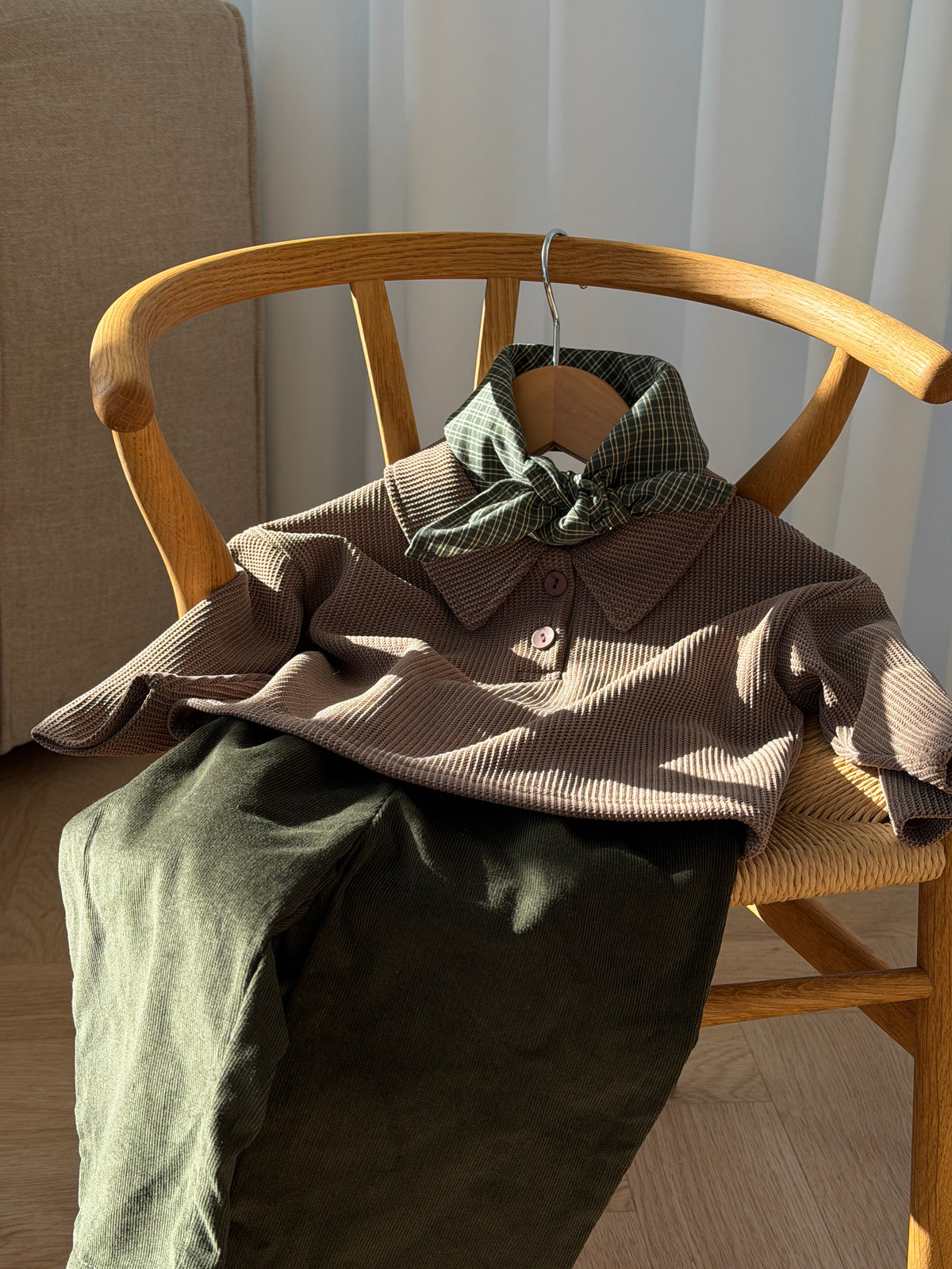 Pine scarf in green check on a brown polo and green trousers on a chair