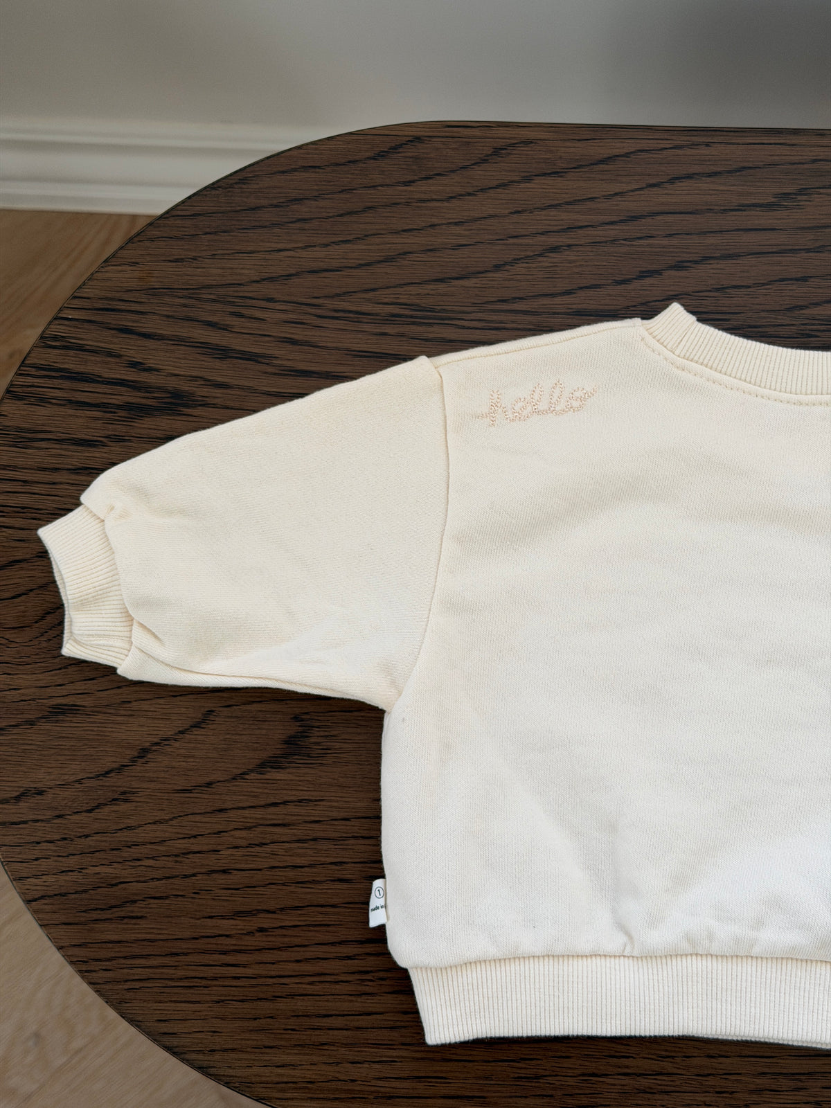 Handpicked cream crew-neck sweatshirt lying on a wooden table