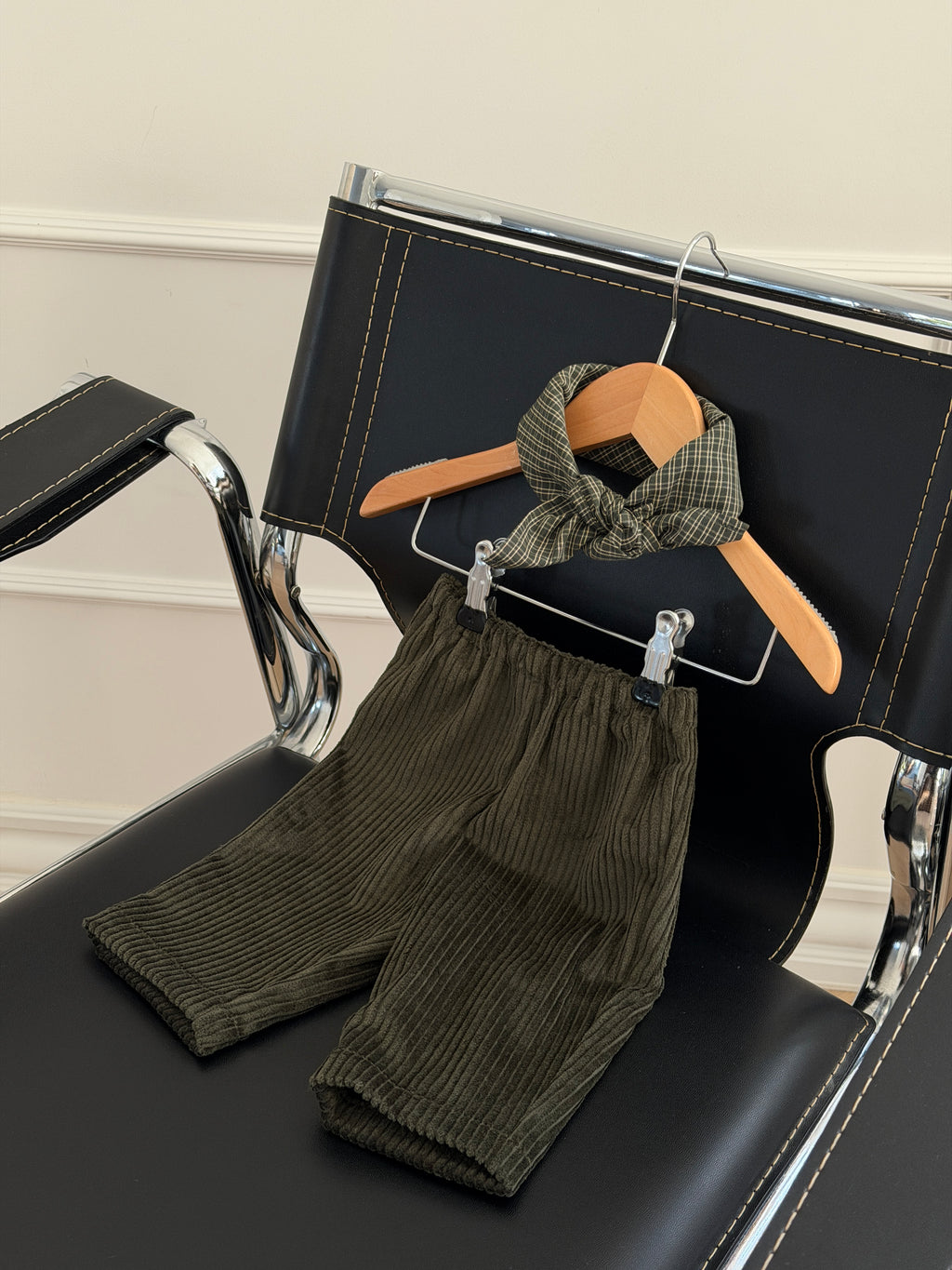 Green velvet trousers and a green checked scarf on a hanger on a black armchair