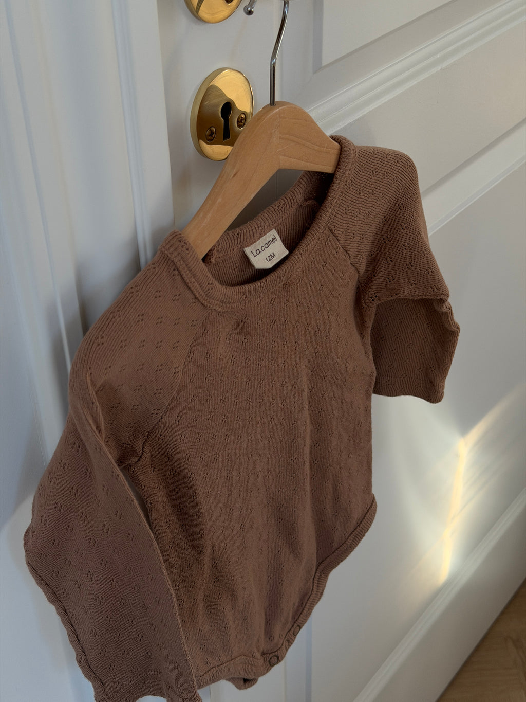 Brown long-sleeved pointelle bodysuit on a hanger on a door