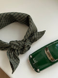 Pine scarf in green check cotton tied in a bow next to a green toy car
