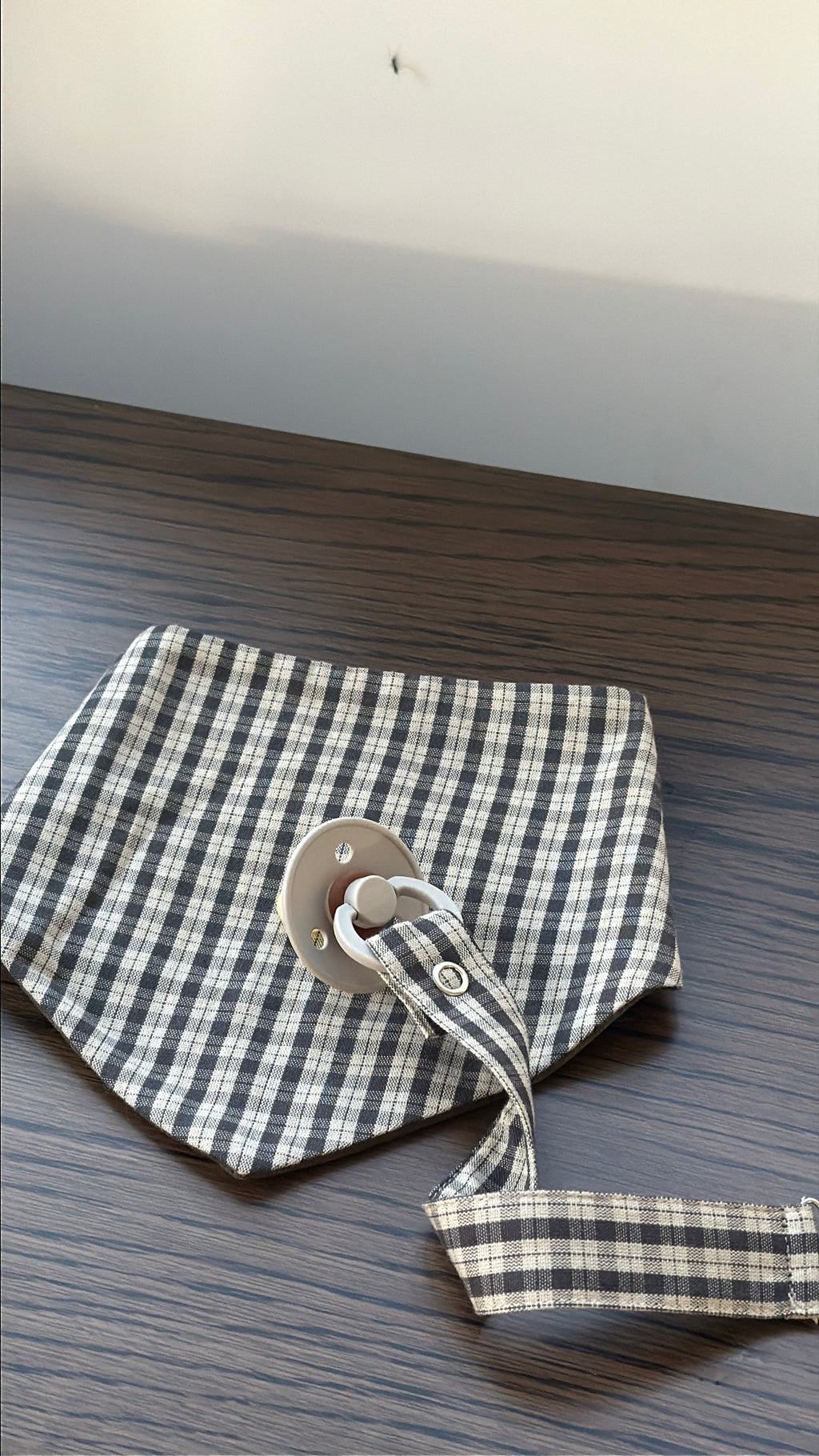 Mocca bib in brown check cotton with dummy clip on a wooden table