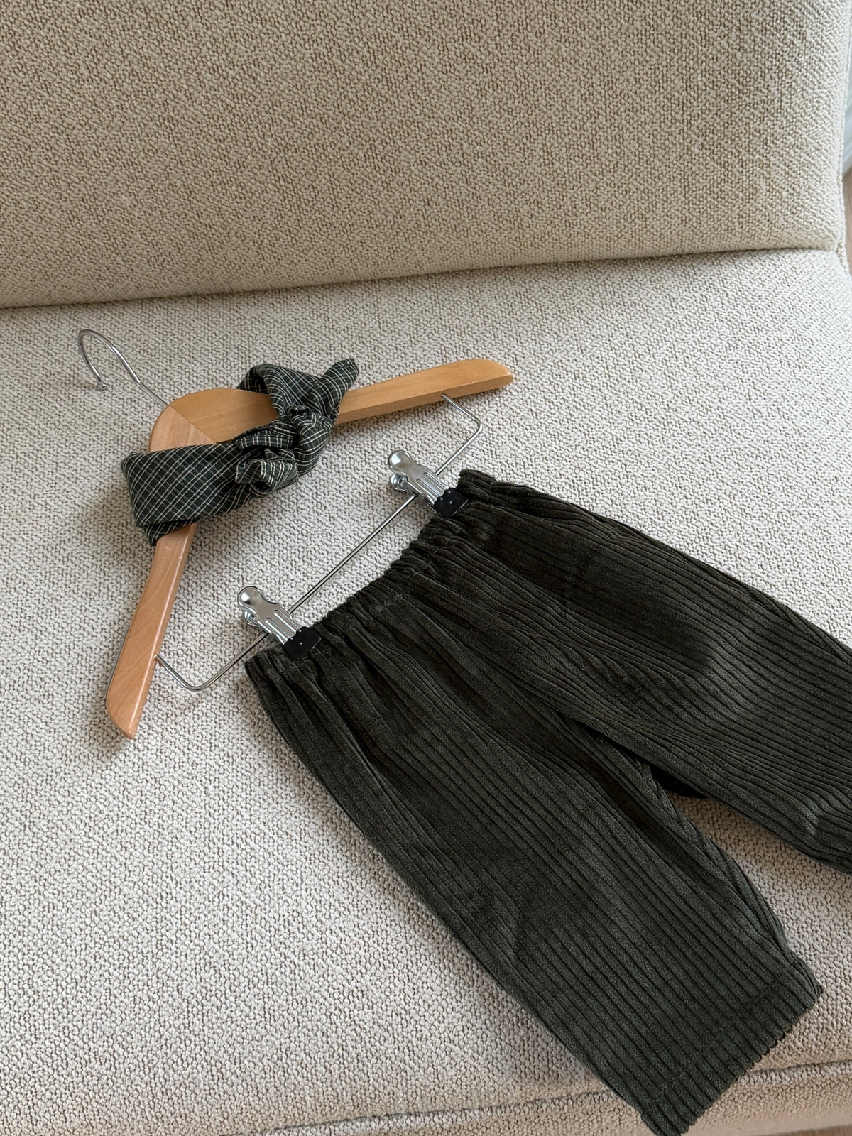 Green velvet trousers and a green checked scarf on a hanger on a beige sofa